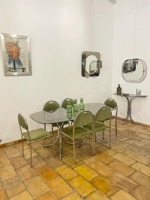 Une table en verre entourée de chaises chromées vert olive, verres verts posés dessus